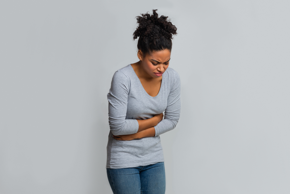 Young african woman touching her belly, suffering from menstrual abdomen cramps