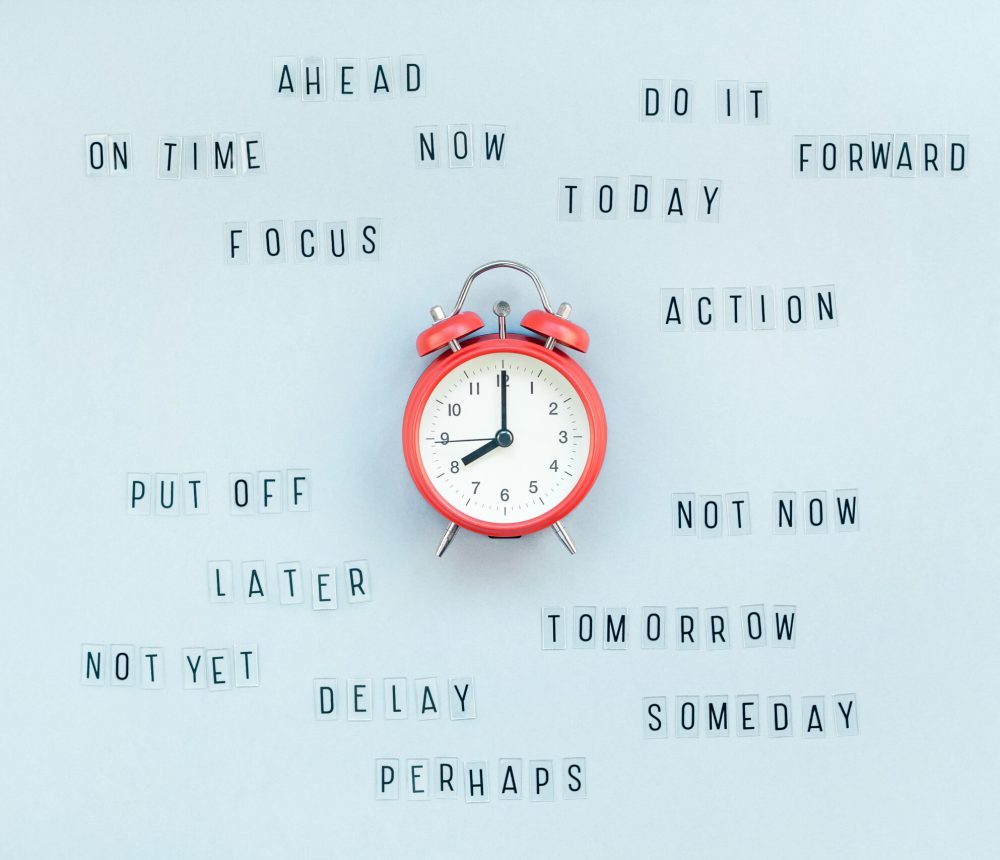 Creative top view flat lay of alarm clock with messages about delay or starting doing task copy space blue background minimal style. Concept of procrastination, time management in business and life