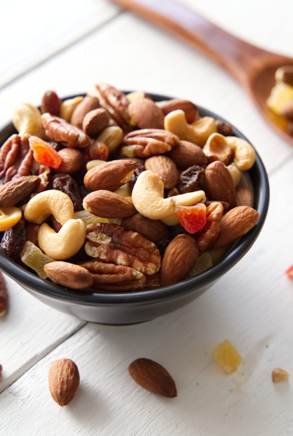 Mix nuts and dried fruits background and wallpaper. Seen in top view of mix nuts and dried fruits in the bowl and wood spoon decorated with some nuts and red leaf on white wood in background.