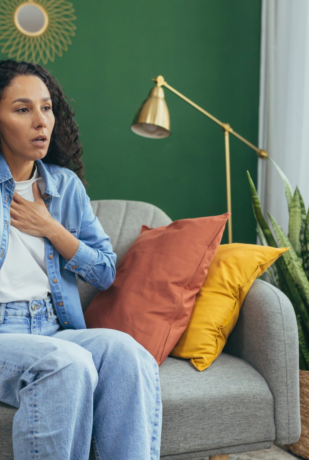 Woman having panic attack, Hispanic woman with curly hair alone at home depressed, having trouble breathing sitting on sofa in living room