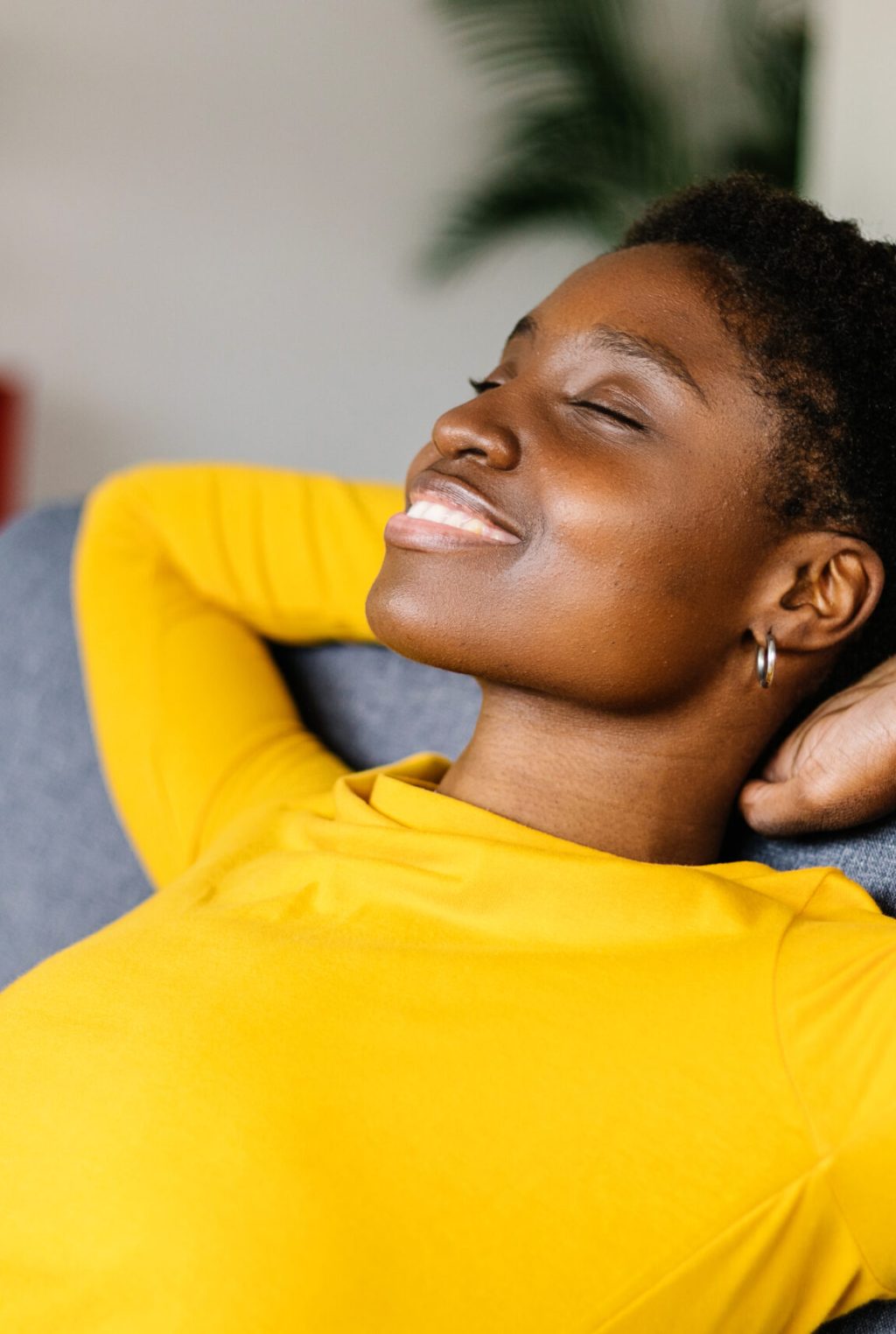 Young African American woman relaxing on a sofa at home - Smiling woman with hands behind head while relaxing on a couch at home.